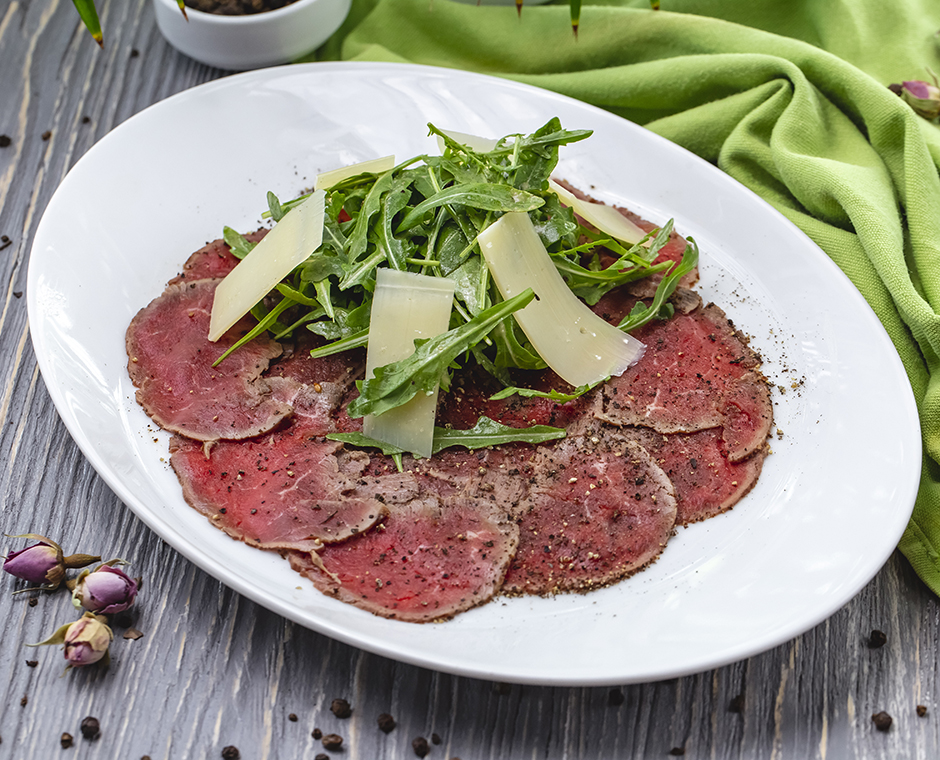 Piatto di carne affumicata sul tavolo con spezie rucola parmigiano vista laterale