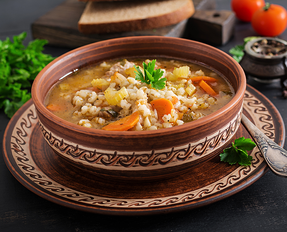 Zuppa d'orzo con carote, pomodoro, sedano e carne su sfondo scuro.
